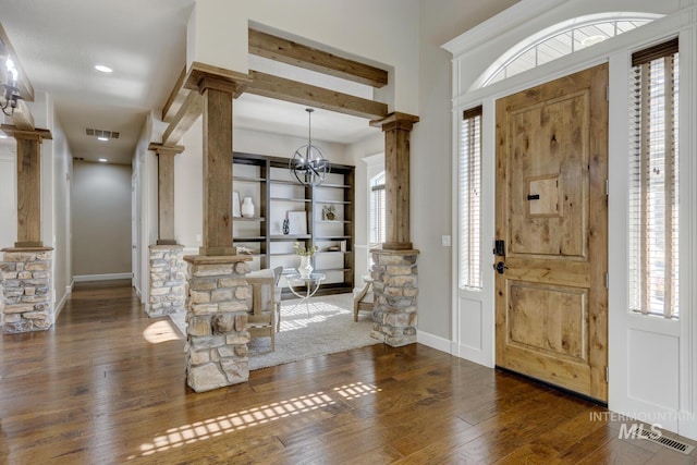 entryway featuring dark wood-type flooring, a notable chandelier, and ornate columns