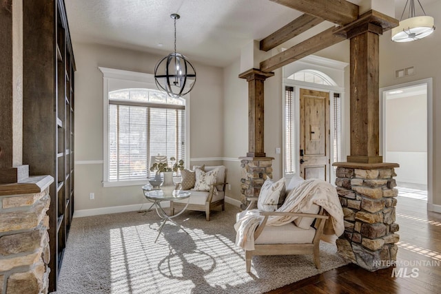 living area with an inviting chandelier, a textured ceiling, dark hardwood / wood-style floors, and ornate columns