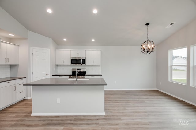 kitchen featuring vaulted ceiling, pendant lighting, white cabinetry, stainless steel appliances, and a center island with sink