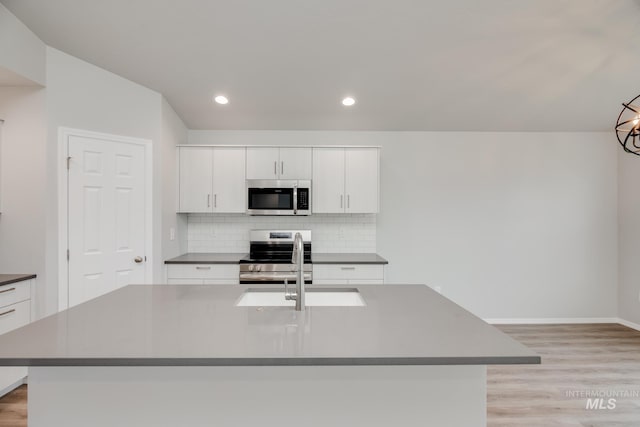 kitchen with white cabinetry, a center island with sink, light wood-type flooring, stainless steel appliances, and decorative backsplash