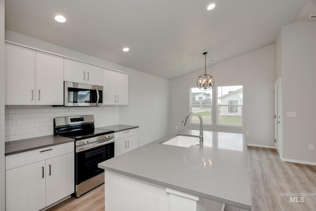 kitchen featuring lofted ceiling, appliances with stainless steel finishes, a kitchen island with sink, backsplash, and hanging light fixtures