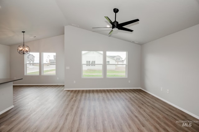 unfurnished living room featuring ceiling fan with notable chandelier, wood-type flooring, and vaulted ceiling