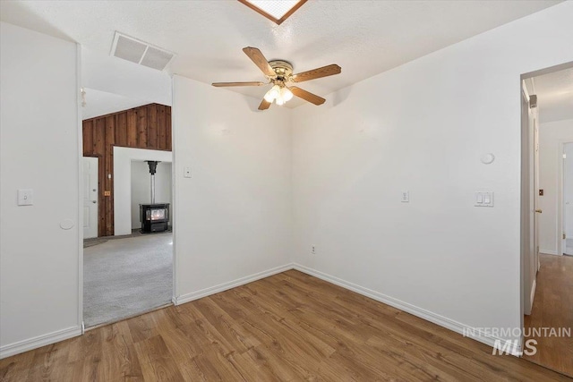 spare room featuring visible vents, ceiling fan, lofted ceiling, a wood stove, and wood finished floors