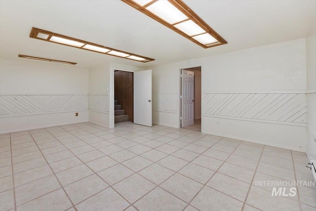 unfurnished room featuring light tile patterned floors, a wainscoted wall, and stairway