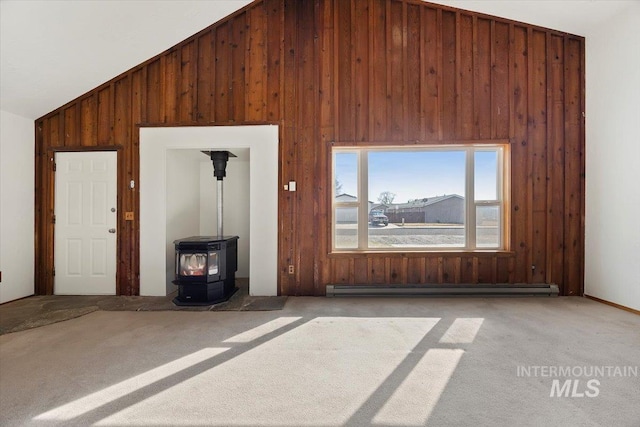 unfurnished living room with baseboard heating, wood walls, a wood stove, and carpet floors