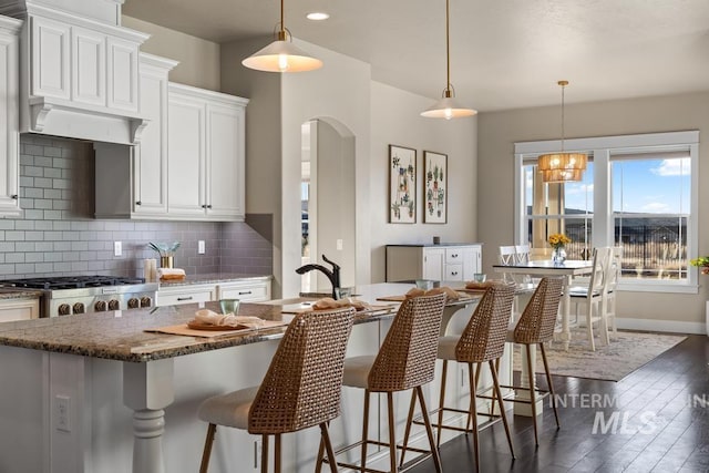 kitchen with dark stone countertops, dark wood-style floors, a sink, stove, and backsplash