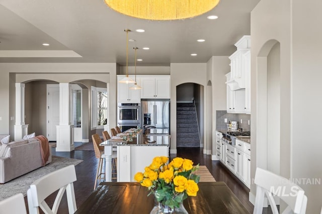 kitchen with dark stone countertops, dark wood-style floors, a breakfast bar, arched walkways, and stainless steel appliances