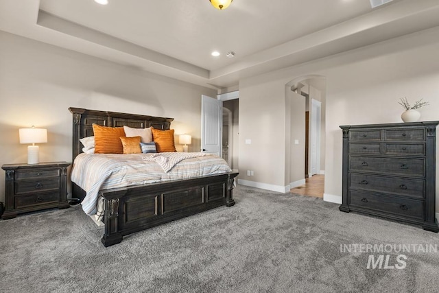 carpeted bedroom with arched walkways, recessed lighting, a tray ceiling, and baseboards