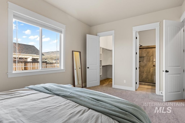 bedroom featuring connected bathroom, a closet, baseboards, light colored carpet, and a spacious closet