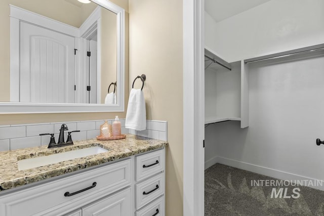 bathroom featuring a walk in closet, baseboards, and vanity