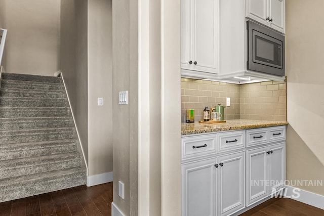 kitchen with light stone countertops, dark wood finished floors, built in microwave, decorative backsplash, and white cabinetry