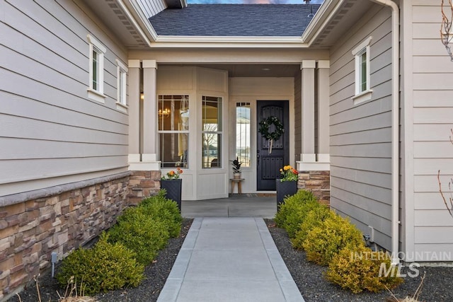 doorway to property featuring stone siding and roof with shingles