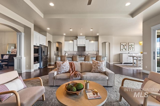 living room featuring recessed lighting, arched walkways, a raised ceiling, and dark wood-style floors