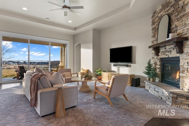 living area with a ceiling fan, recessed lighting, arched walkways, a fireplace, and a raised ceiling