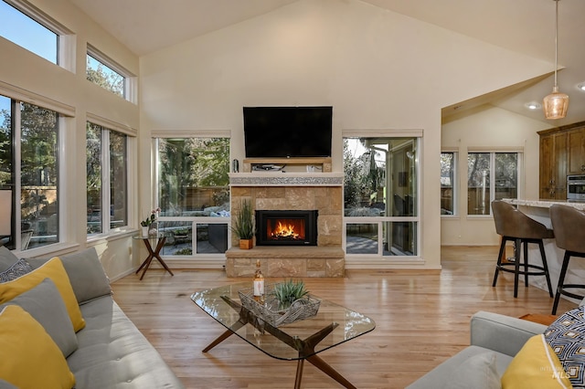 living room with a stone fireplace, high vaulted ceiling, light wood-type flooring, baseboards, and recessed lighting