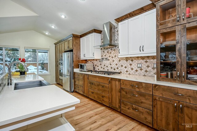kitchen featuring stainless steel appliances, wall chimney range hood, a sink, vaulted ceiling, and tasteful backsplash
