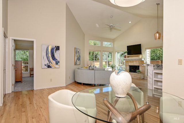 living room featuring high vaulted ceiling, a ceiling fan, a fireplace with raised hearth, light wood-style floors, and baseboards