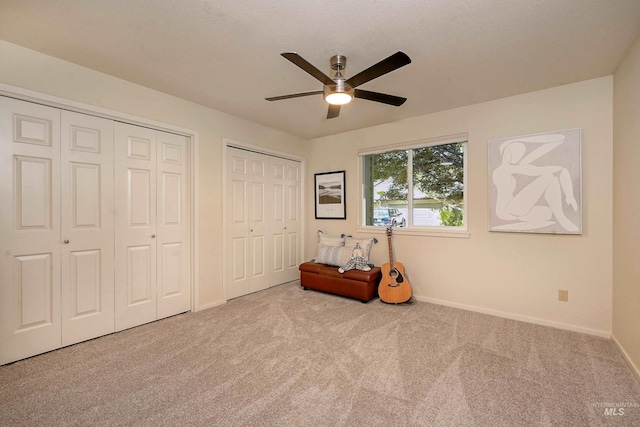 unfurnished bedroom with carpet flooring, two closets, baseboards, and a ceiling fan
