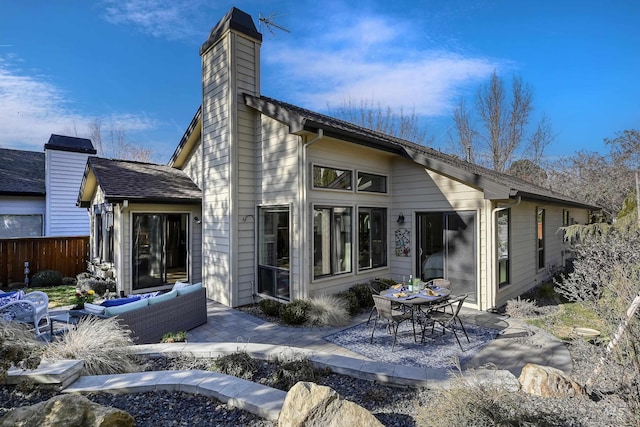 rear view of property featuring a patio, outdoor lounge area, a chimney, and fence