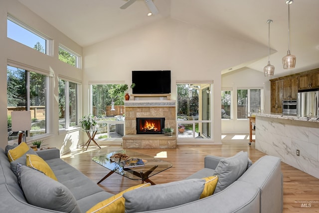 living room with high vaulted ceiling, a fireplace, a ceiling fan, and light wood-style floors