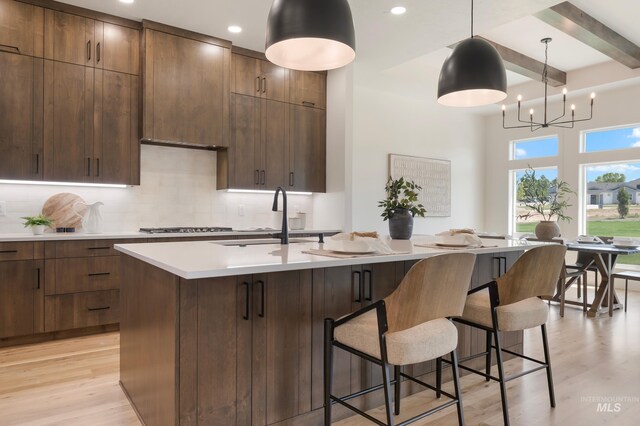 24910 Ardmore Ct, Caldwell, ID 83607 - kitchen featuring light wood finished floors, light countertops, a kitchen bar, backsplash, and beamed ceiling