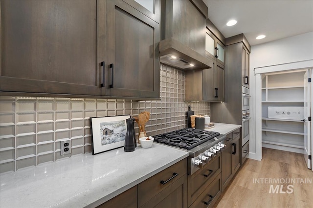 kitchen with light stone countertops, light hardwood / wood-style floors, appliances with stainless steel finishes, tasteful backsplash, and wall chimney exhaust hood