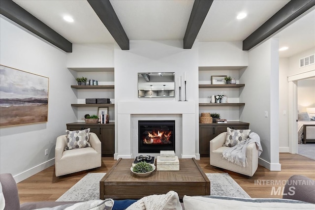 living room with built in features, beam ceiling, and hardwood / wood-style floors