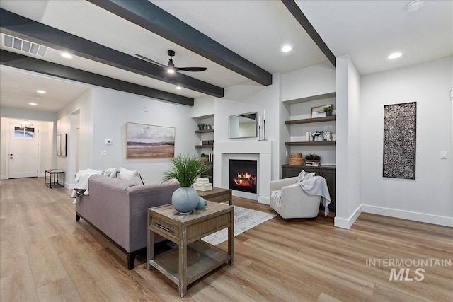 living room featuring built in shelves, light hardwood / wood-style flooring, beam ceiling, and ceiling fan