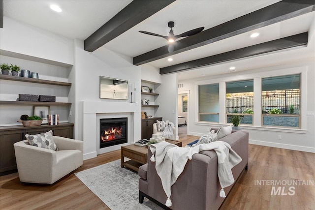 living room with ceiling fan, built in features, beamed ceiling, and light hardwood / wood-style flooring