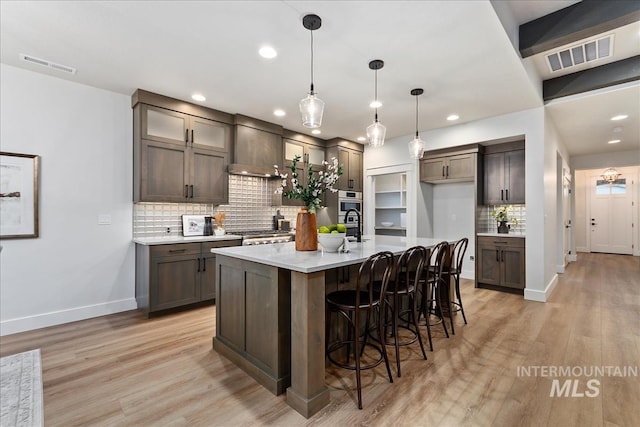 kitchen featuring wall chimney exhaust hood, backsplash, a kitchen island with sink, and decorative light fixtures