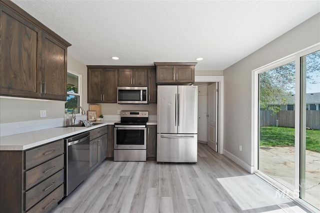 kitchen featuring appliances with stainless steel finishes, dark brown cabinets, a sink, light countertops, and light wood finished floors