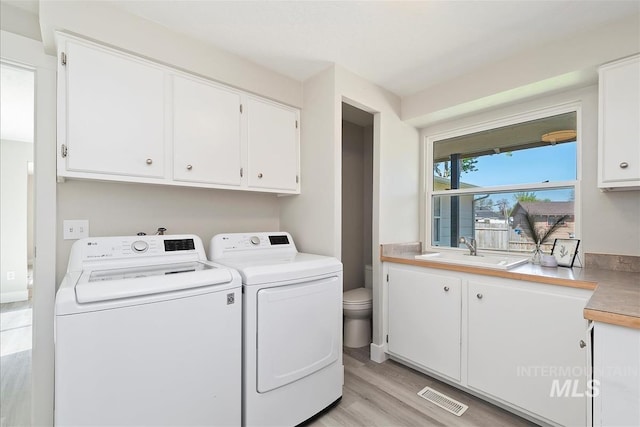 washroom with cabinet space, a sink, separate washer and dryer, light wood-type flooring, and visible vents