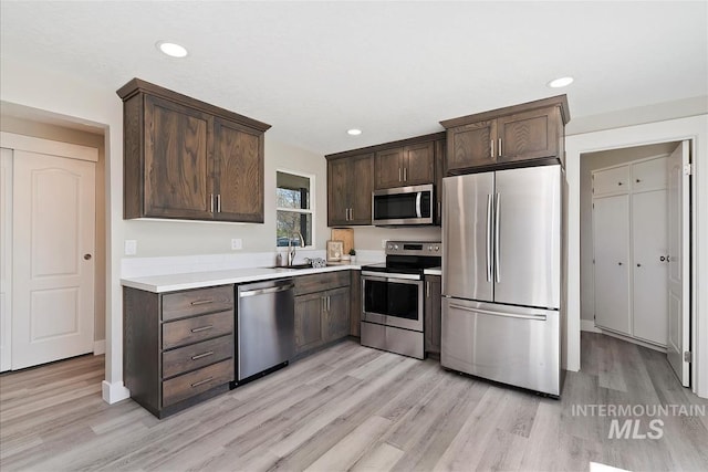 kitchen with dark brown cabinetry, appliances with stainless steel finishes, a sink, light countertops, and light wood-style flooring