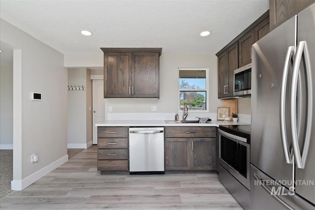 kitchen with light countertops, stainless steel appliances, dark brown cabinetry, and a sink