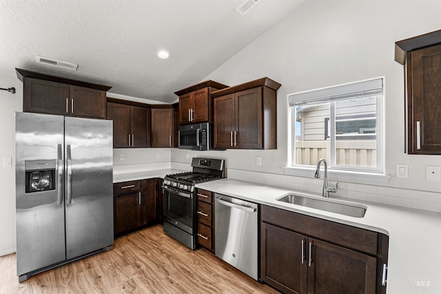 kitchen with stainless steel appliances, vaulted ceiling, a sink, light wood-style flooring, and dark brown cabinets
