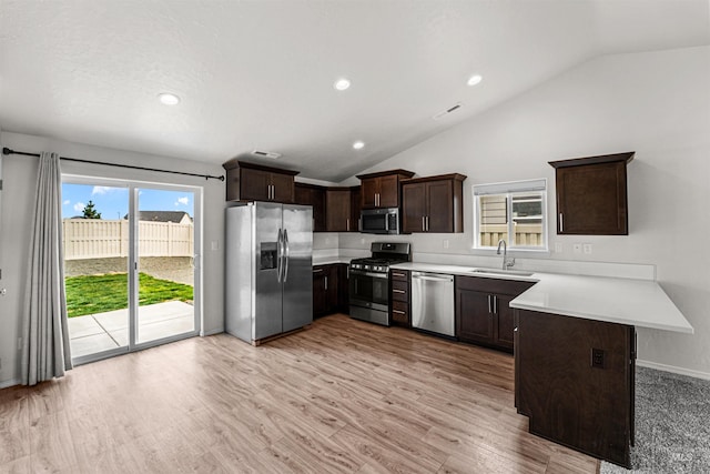 kitchen featuring appliances with stainless steel finishes, a sink, a peninsula, dark brown cabinets, and lofted ceiling
