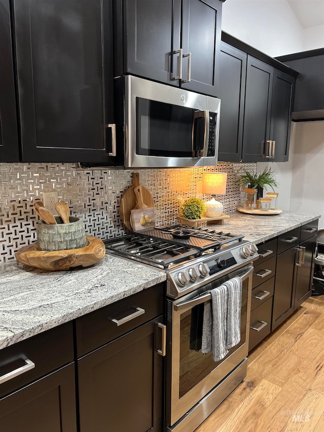 kitchen with light wood-type flooring, appliances with stainless steel finishes, decorative backsplash, and light stone counters