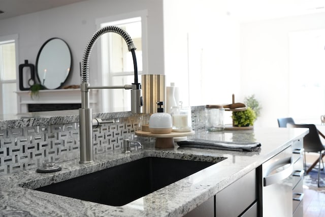 room details with stainless steel dishwasher, sink, light stone counters, and decorative backsplash