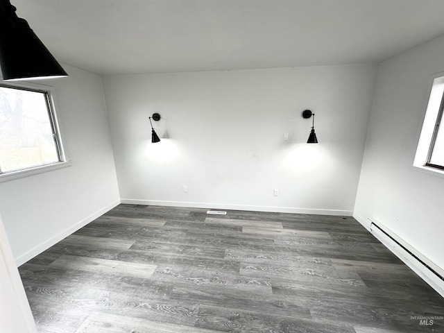 spare room featuring dark hardwood / wood-style flooring, baseboard heating, and a healthy amount of sunlight