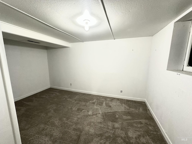 basement featuring a textured ceiling and dark colored carpet