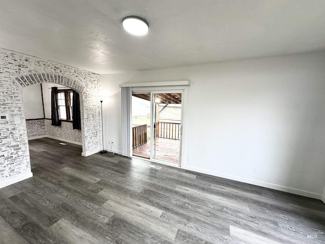 unfurnished room with dark wood-type flooring and brick wall