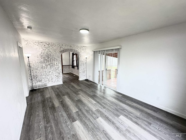 spare room featuring dark hardwood / wood-style floors and brick wall