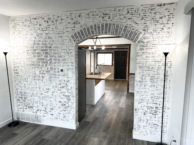 corridor with a chandelier, dark hardwood / wood-style flooring, brick wall, and sink