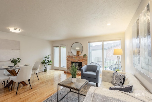 living room featuring a brick fireplace, plenty of natural light, light wood finished floors, and a textured ceiling