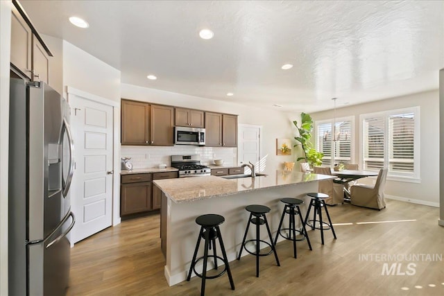 kitchen with a kitchen island with sink, decorative backsplash, decorative light fixtures, stainless steel appliances, and a breakfast bar area