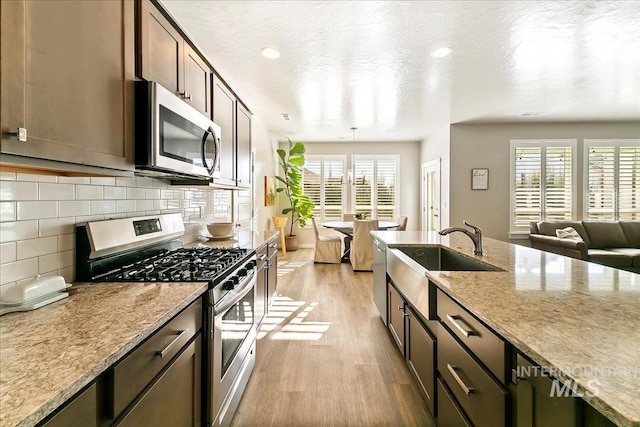 kitchen with sink, dark brown cabinetry, light hardwood / wood-style flooring, stainless steel appliances, and light stone counters