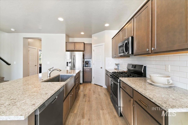 kitchen featuring stainless steel appliances, an island with sink, light hardwood / wood-style floors, decorative backsplash, and light stone counters