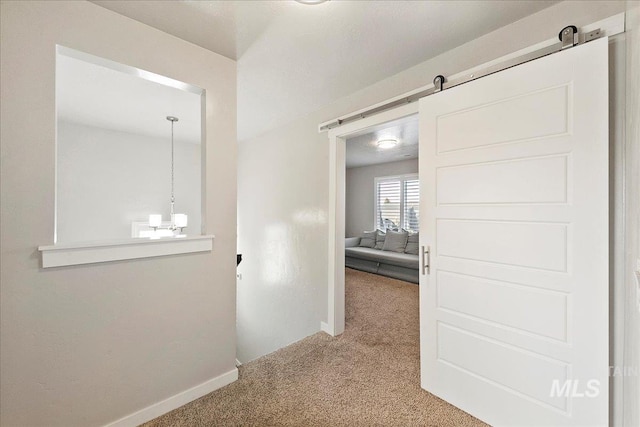 hallway with an inviting chandelier, a barn door, and carpet flooring