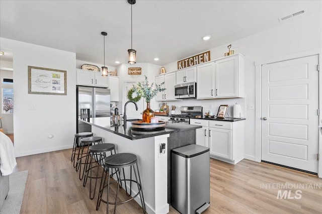 1499 W Blue Downs St, Meridian, ID 83642 - kitchen with appliances with stainless steel finishes, dark countertops, a kitchen bar, light wood-style flooring, and decorative light fixtures