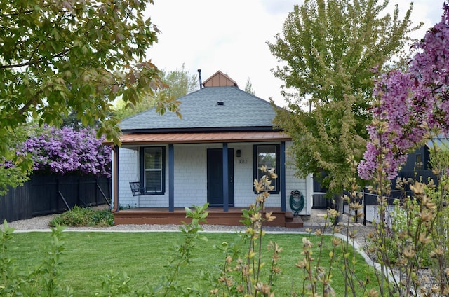 view of front of home with covered porch, fence, roof with shingles, and a front lawn